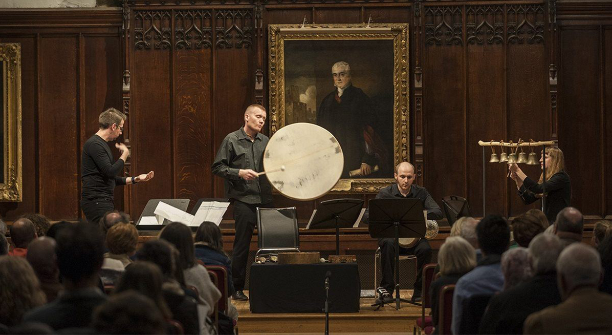 Four musicians performing with percussion instruments in wood panelled room 